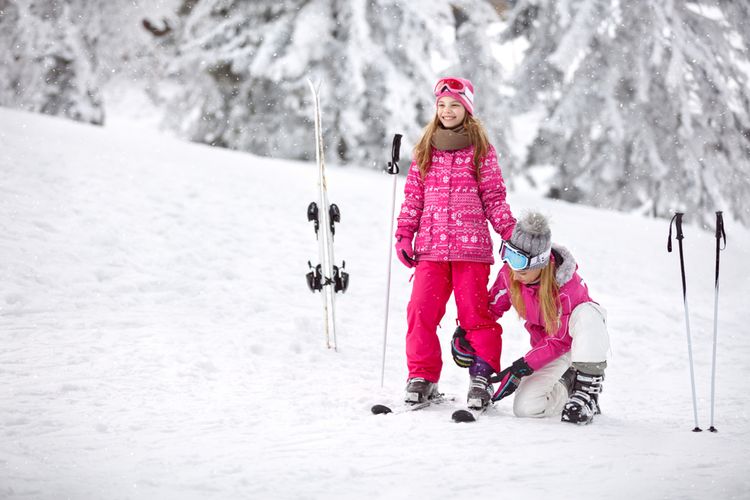 Matka pomáha dcére pripevniť lyžiarku o lyže